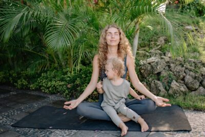 A mother meditating outdoors while her child sits on her lap